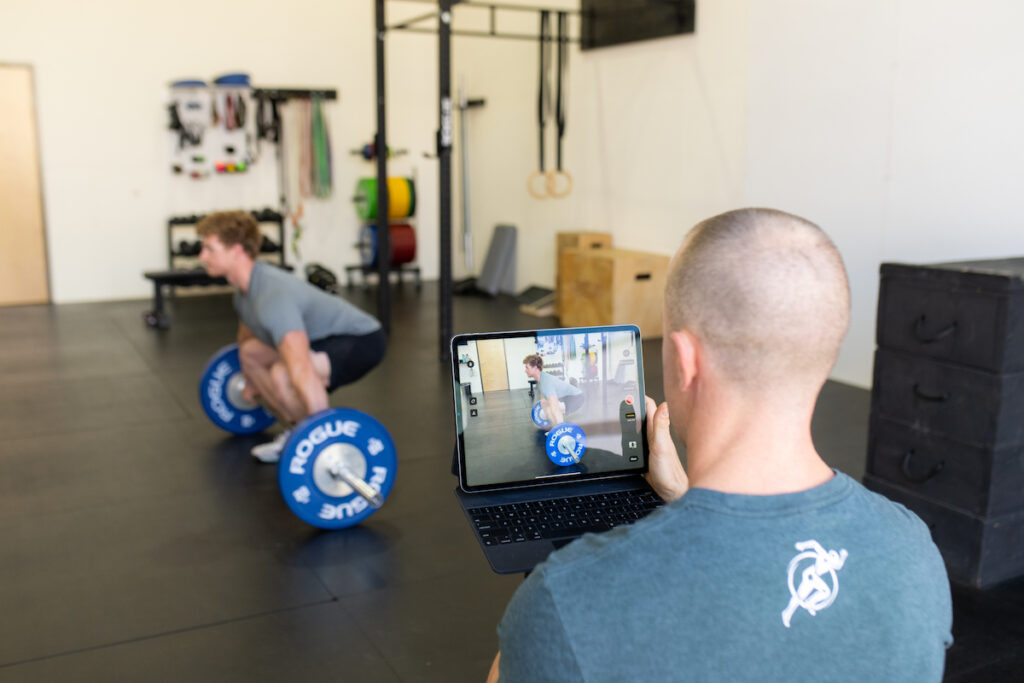 A man using a laptop to take a picture of a barbell in a gym.