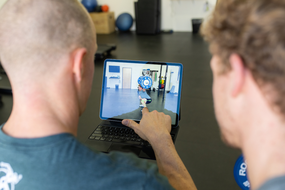 Two men in a gym looking at a video on a laptop.
