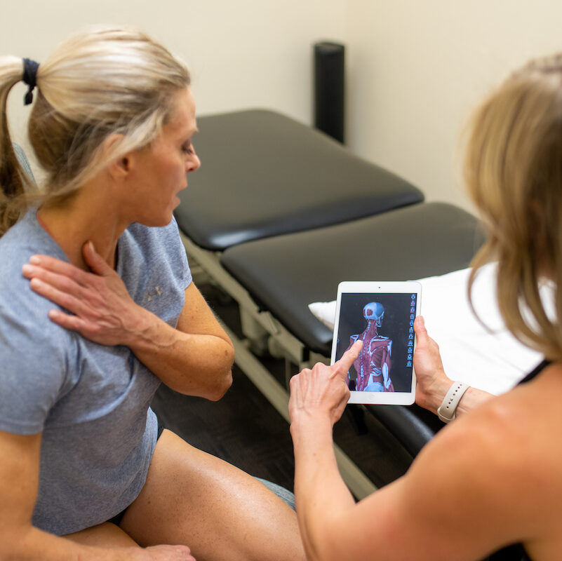 A woman is looking at an ipad while sitting on a massage table.