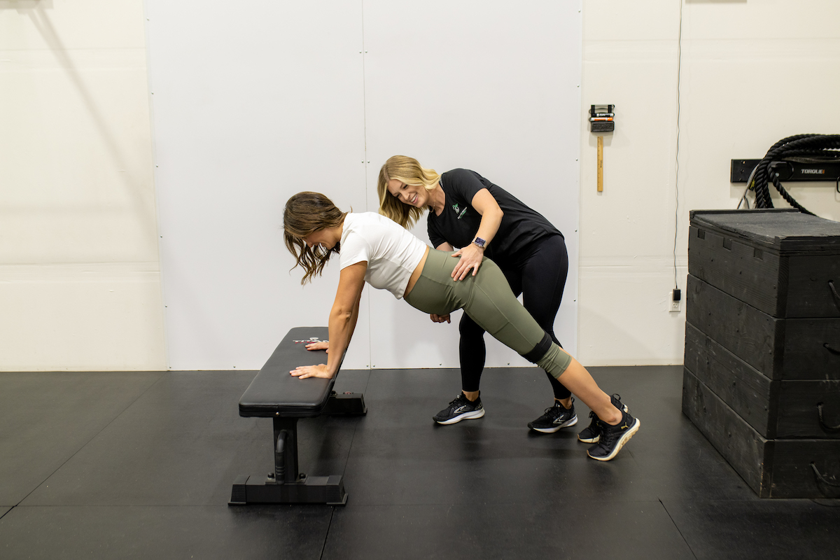 Two women doing squats on a bench in a gym.