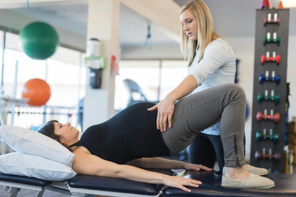 A pregnant woman is being helped by a physical therapist.