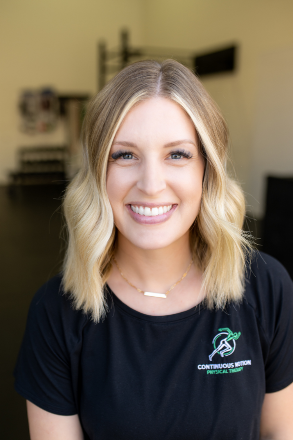 A woman in a black t - shirt smiling in front of a gym.